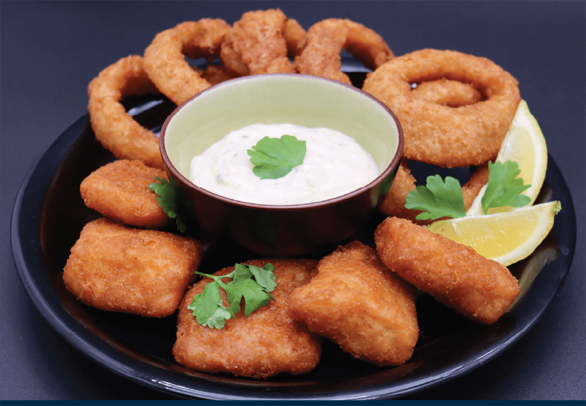 Lil' Haddies shown on a plate with onion rings and wedges of lemon and dipping sauce
